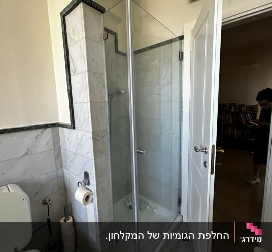 מקלחון זכוכית עם בקבוקי שמפו על הרצפה
